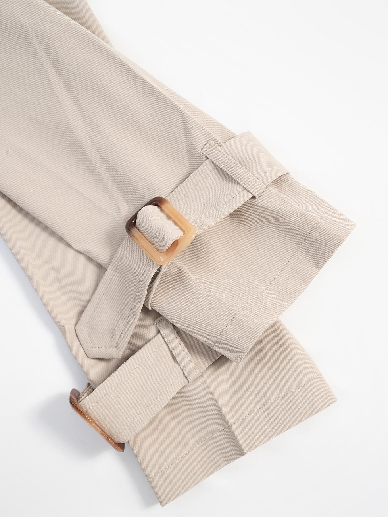 Beige cropped trench coat detail showing adjustable cuffs with tortoise shell buckles.
