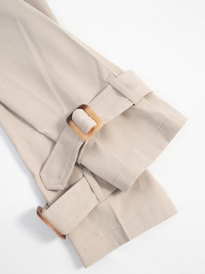 Beige cropped trench coat detail showing adjustable cuffs with tortoise shell buckles.