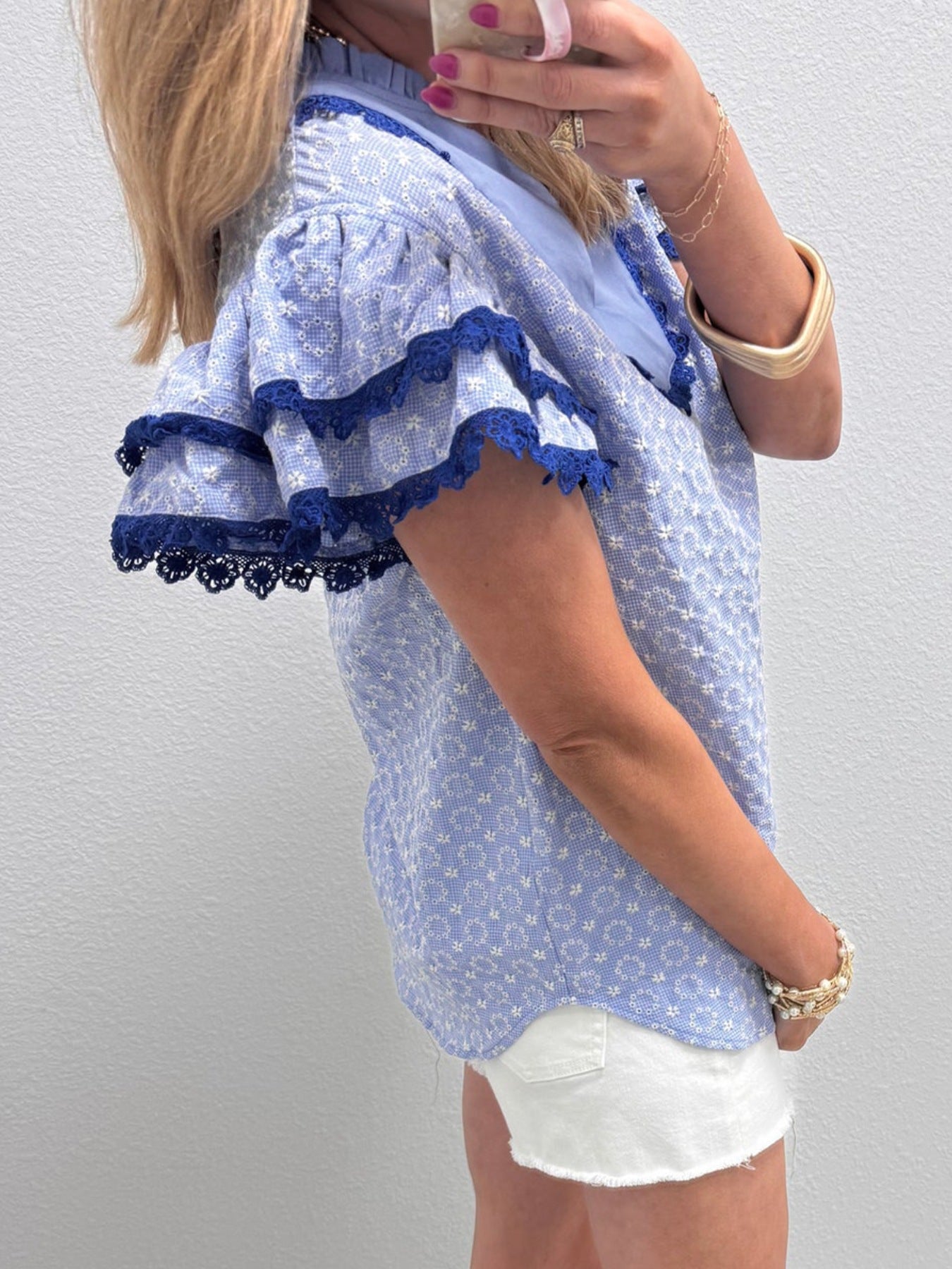 Light blue eyelet embroidered blouse with flutter sleeves and navy lace trim.