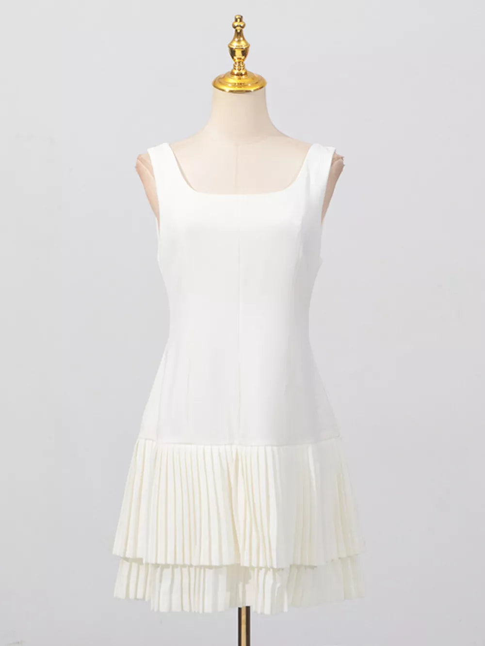 White square neck sleeveless mini dress with layered pleated hem detail.