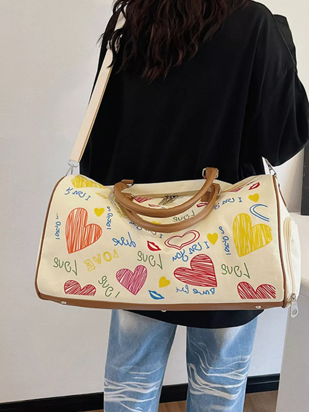 Vibrant canvas duffel bag with colorful heart print, brown trim, and adjustable strap.