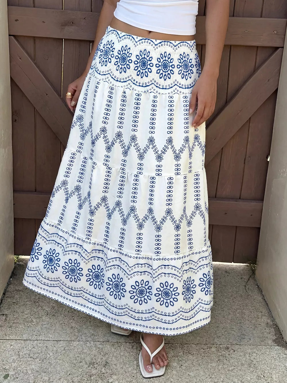 Bohemian white maxi skirt with blue floral embroidery and tiered ruffles.