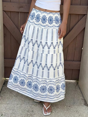 Bohemian white maxi skirt with blue floral embroidery and tiered ruffles.