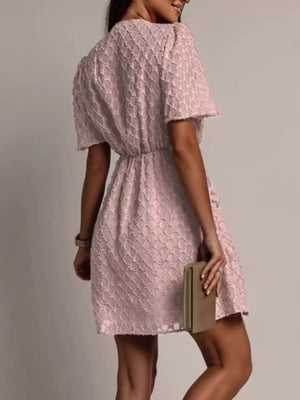 Pink textured V-neck ruched mini dress with short sleeves and cinched waist.