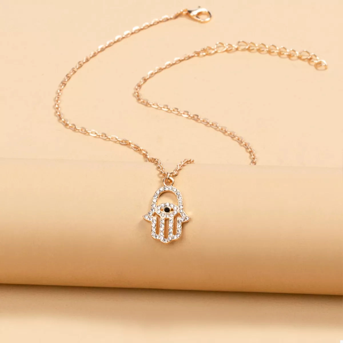Gold evil eye Hamsa hand necklace with clear rhinestones and a black eye detail.