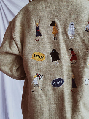 Tan knit sweater with embroidered characters and speech bubbles, relaxed fit.