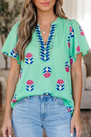 Embroidered floral V-neck blouse with flutter sleeves in light green with pink and blue details.