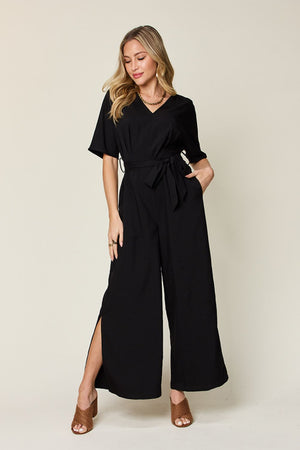 Black wrap jumpsuit with V-neck, short sleeves, tie waist, and slit wide legs.