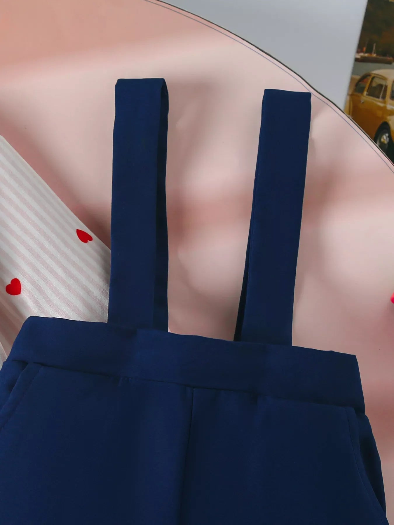 Navy suspender pants with a white and pink striped bodysuit featuring red hearts.