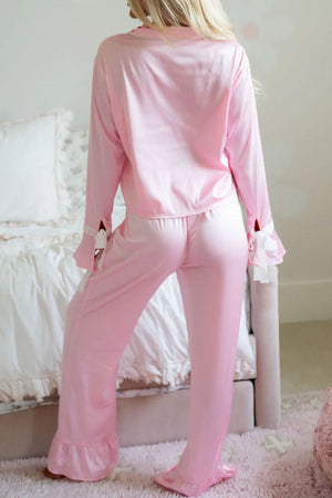 Blush pink silk pajama set with ruffle trim on collar, cuffs, and pant legs.