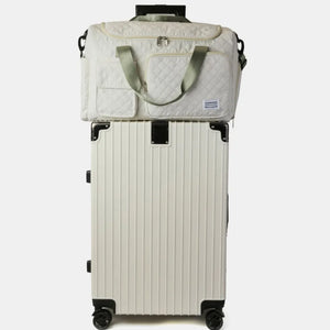 White quilted duffel bag with olive accents on top of a white ribbed suitcase.