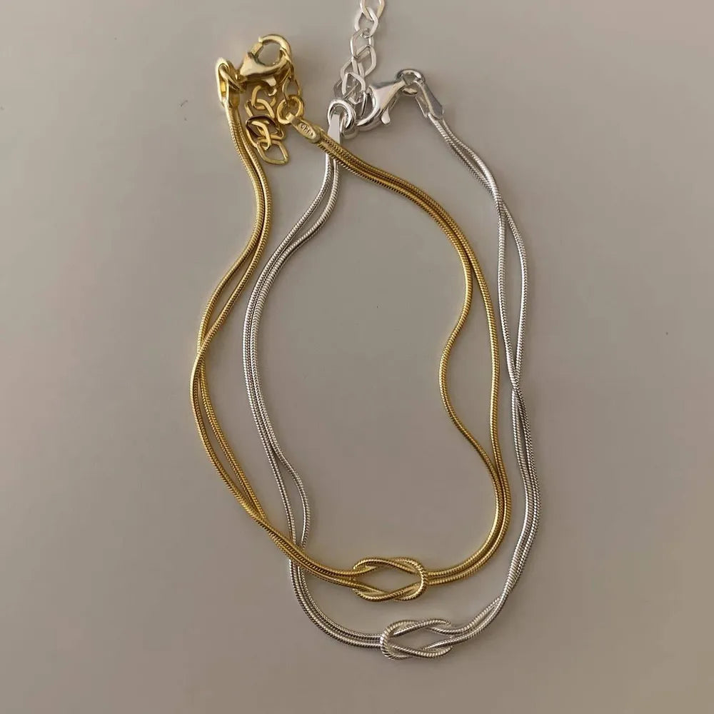Two-tone serpent knot necklaces in gold and silver with snake chains.