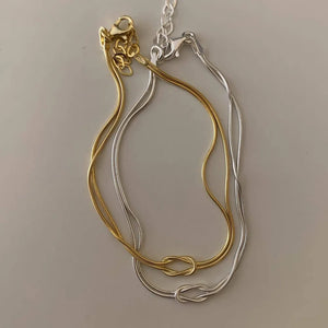 Two-tone serpent knot necklaces in gold and silver with snake chains.