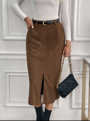 Brown corduroy midi skirt with front slit and pockets, styled with a belt and chain bag.