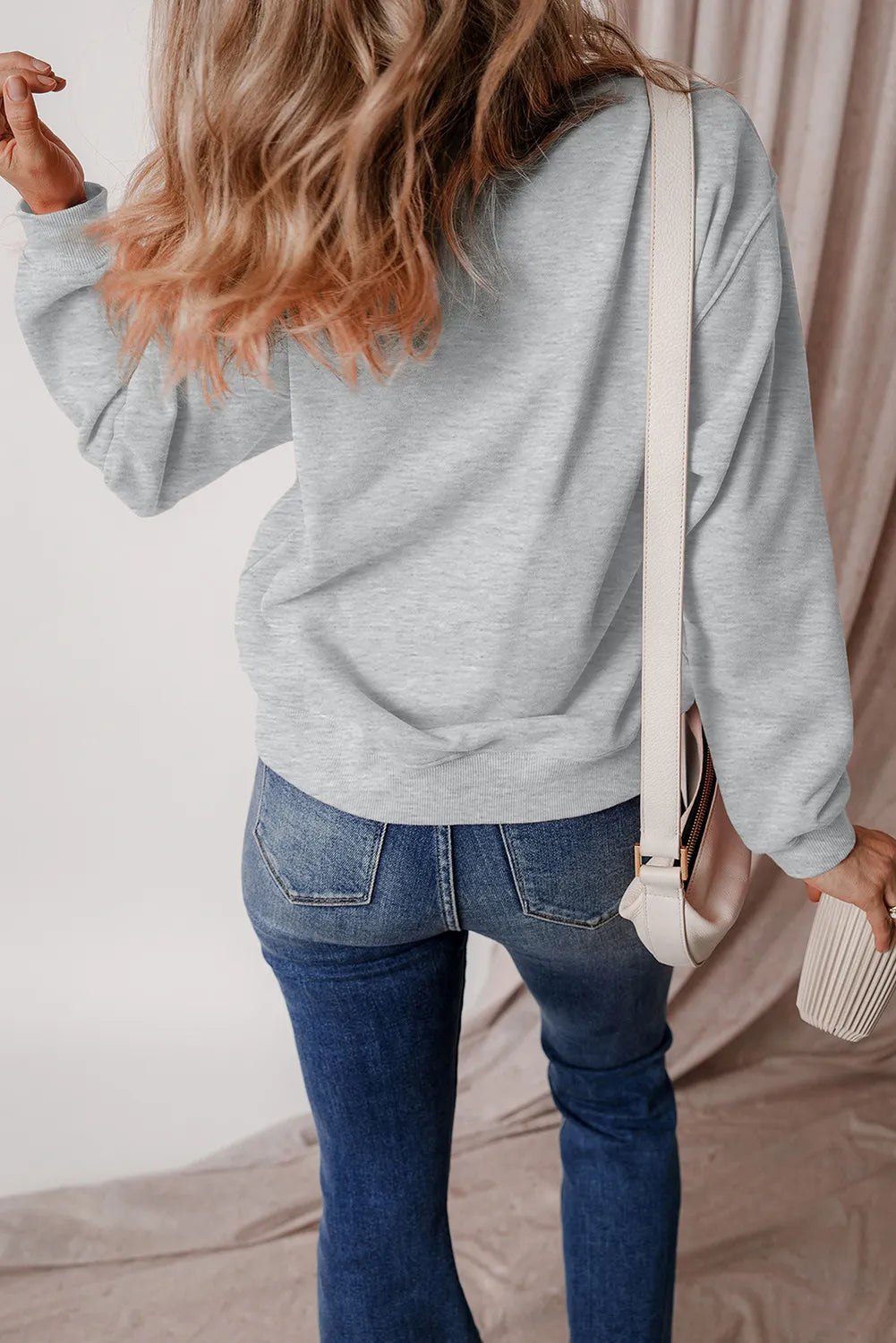 Gray crewneck sweatshirt with long sleeves and ribbed cuffs, styled with jeans.