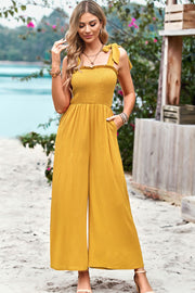 Gold smocked bodice tie-strap palazzo jumpsuit with wide legs and pockets.