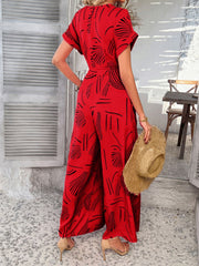 Red geometric print wide-leg jumpsuit with short sleeves and a belted waist.