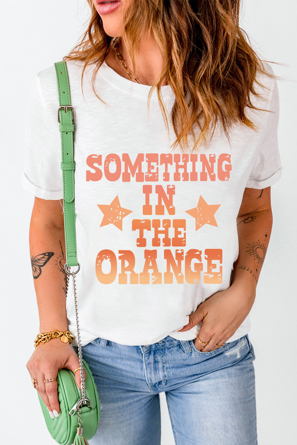 White graphic tee with faded orange text and stars reading "SOMETHING IN THE ORANGE