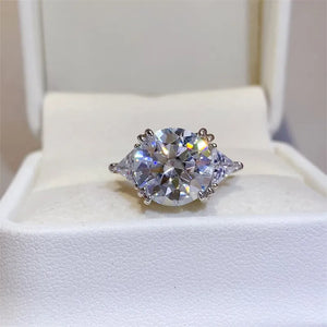 Sterling silver ring with a large, brilliant round moissanite center stone flanked by two trillion-cut moissanite stones.