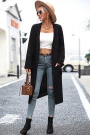 Longline knit cardigan in black with pockets, worn open over a white crop top and jeans.