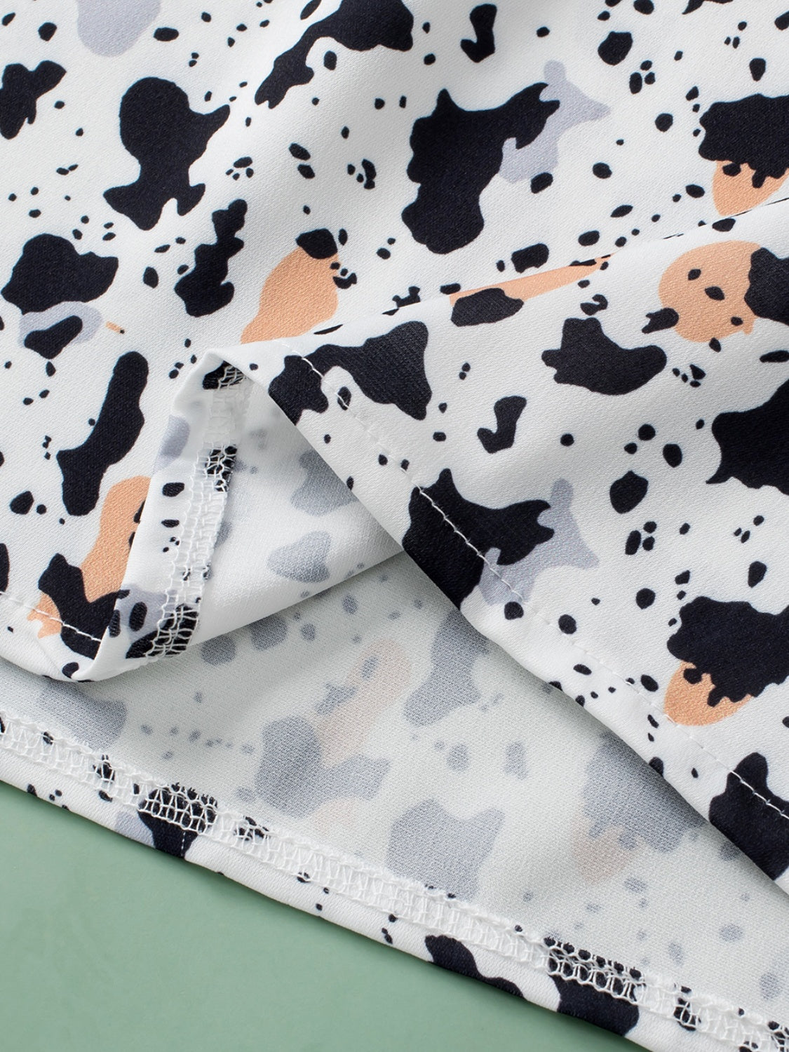 White blouse with black, grey, and peach terrazzo print and ruffle yoke detail.