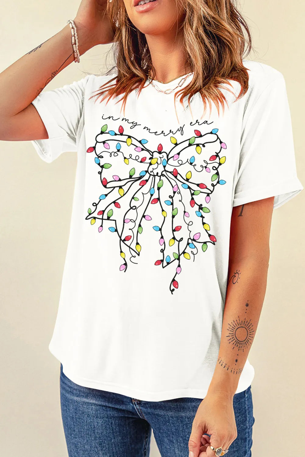 White graphic tee with holiday lights bow and "in my merry era" text