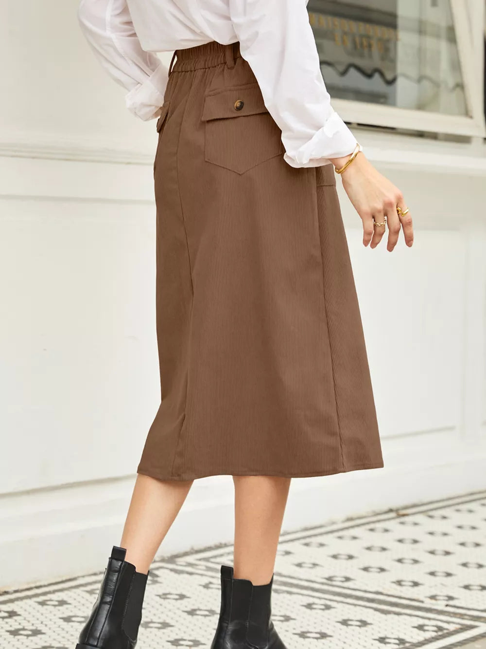 Brown midi skirt with elastic waist, buttoned pocket detail, and subtle vertical ribbing.