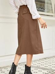 Brown midi skirt with elastic waist, buttoned pocket detail, and subtle vertical ribbing.