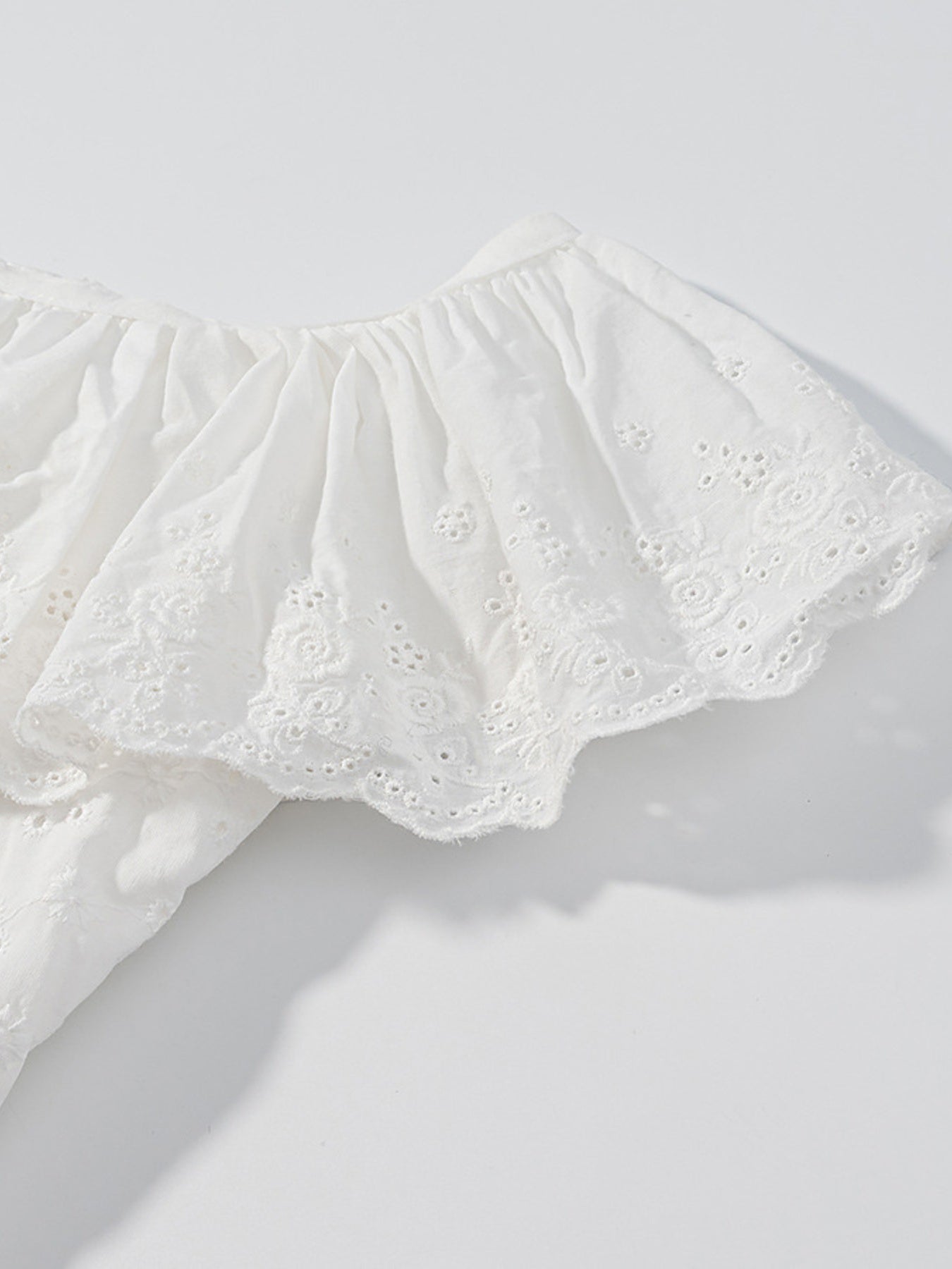 White eyelet tank top with ruffled trim and floral embroidery detail.