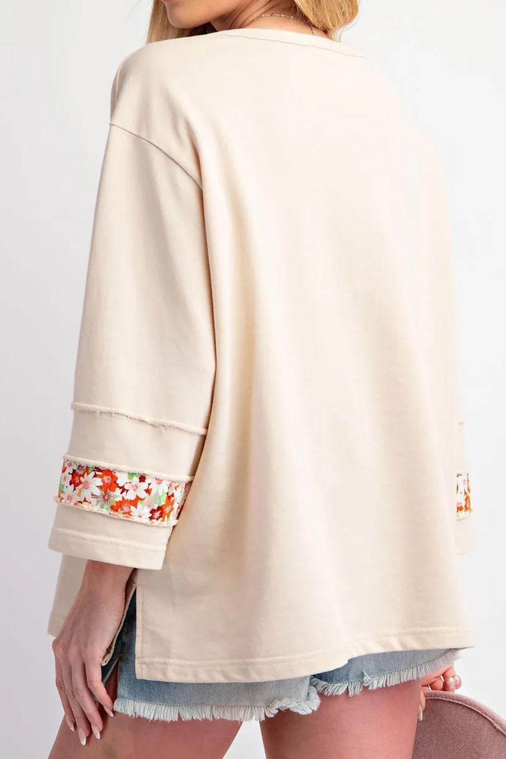 Ivory sweatshirt with floral appliqué raglan sleeves and raw hem details.