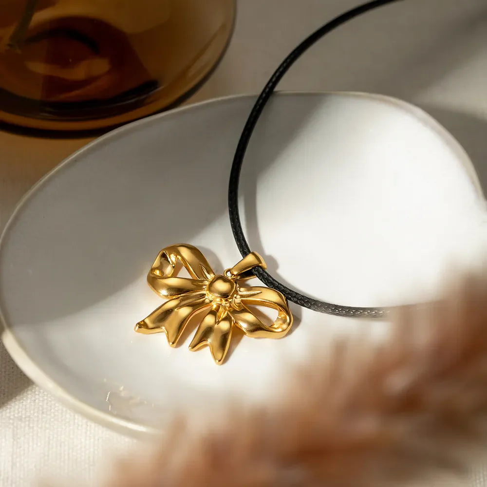 Gold sculptural bow pendant necklace on black wax rope, 18K gold-plated charm