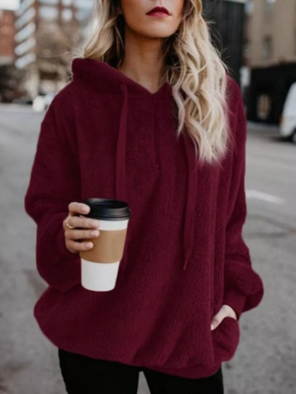 Burgundy plush fleece hoodie with drawstring and pockets, worn by a woman holding coffee.