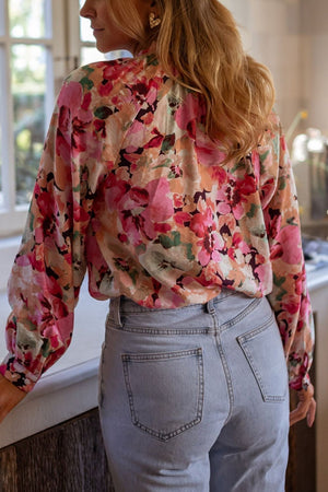 Floral print blouse with ruffle yoke and long sleeves in pink, paired with light wash jeans.