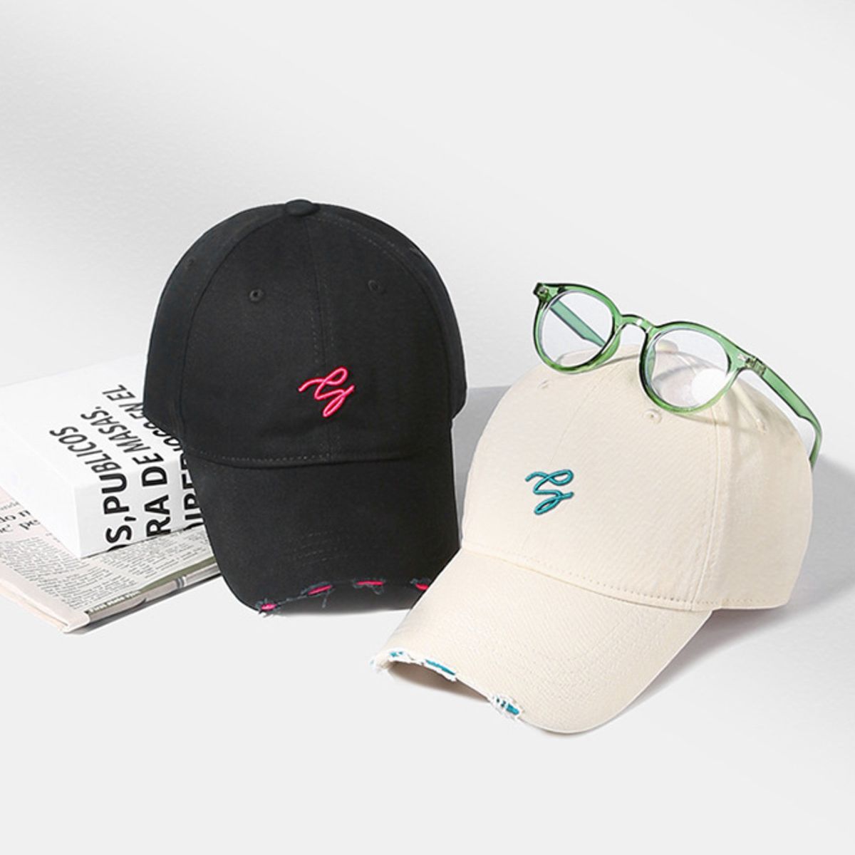 Distressed cotton baseball caps in off-white and black with embroidered logos and frayed details.