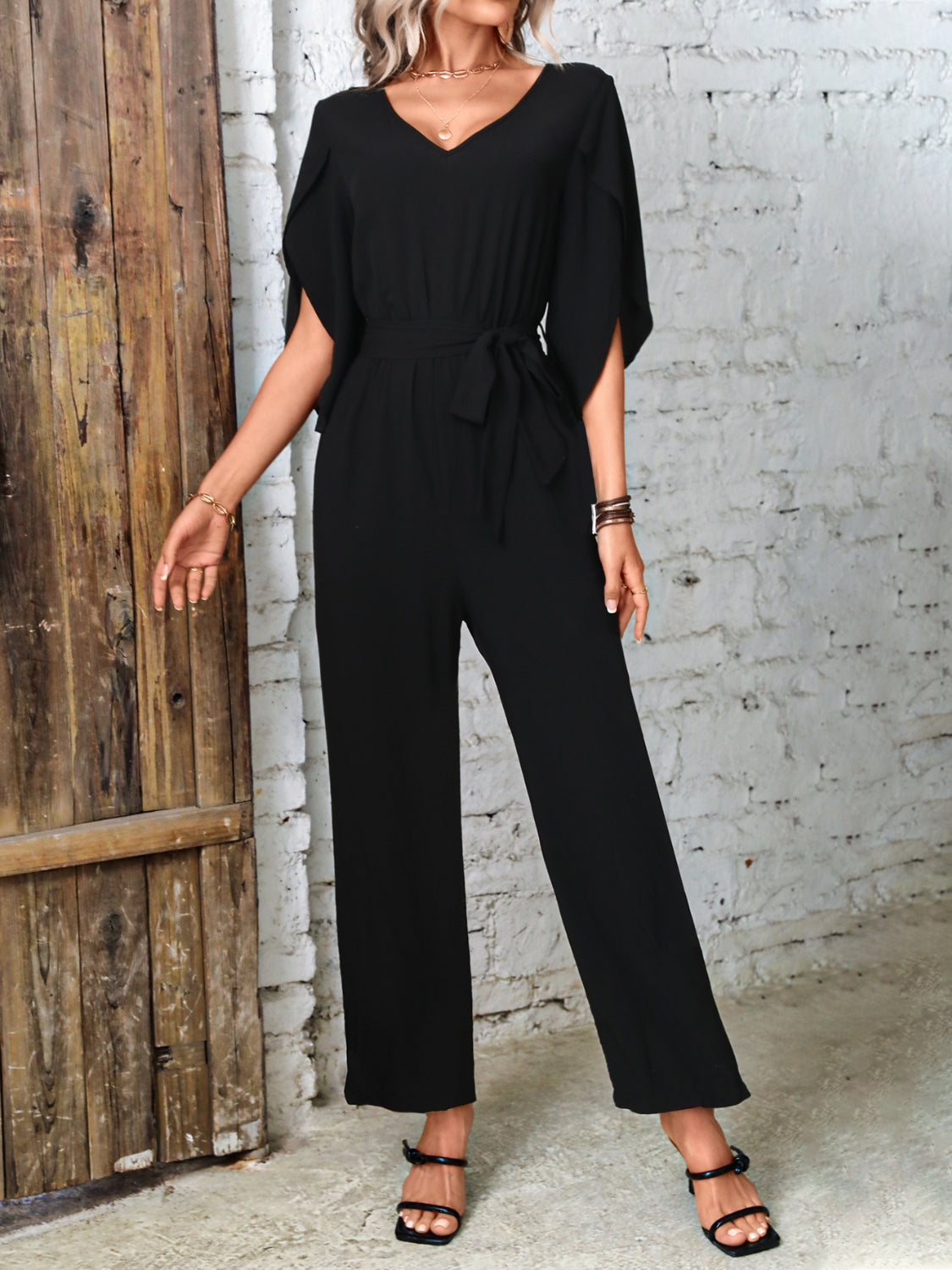 Black cape sleeve wrap jumpsuit with tie waist and wide legs.