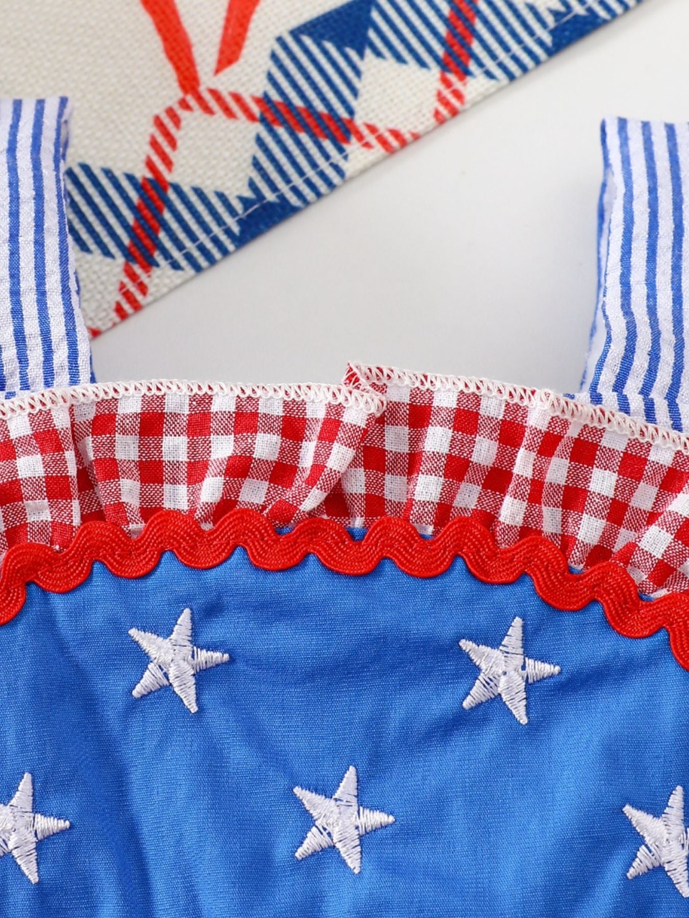 Patriotic baby dress with blue star embroidery, red gingham ruffles, and striped straps.