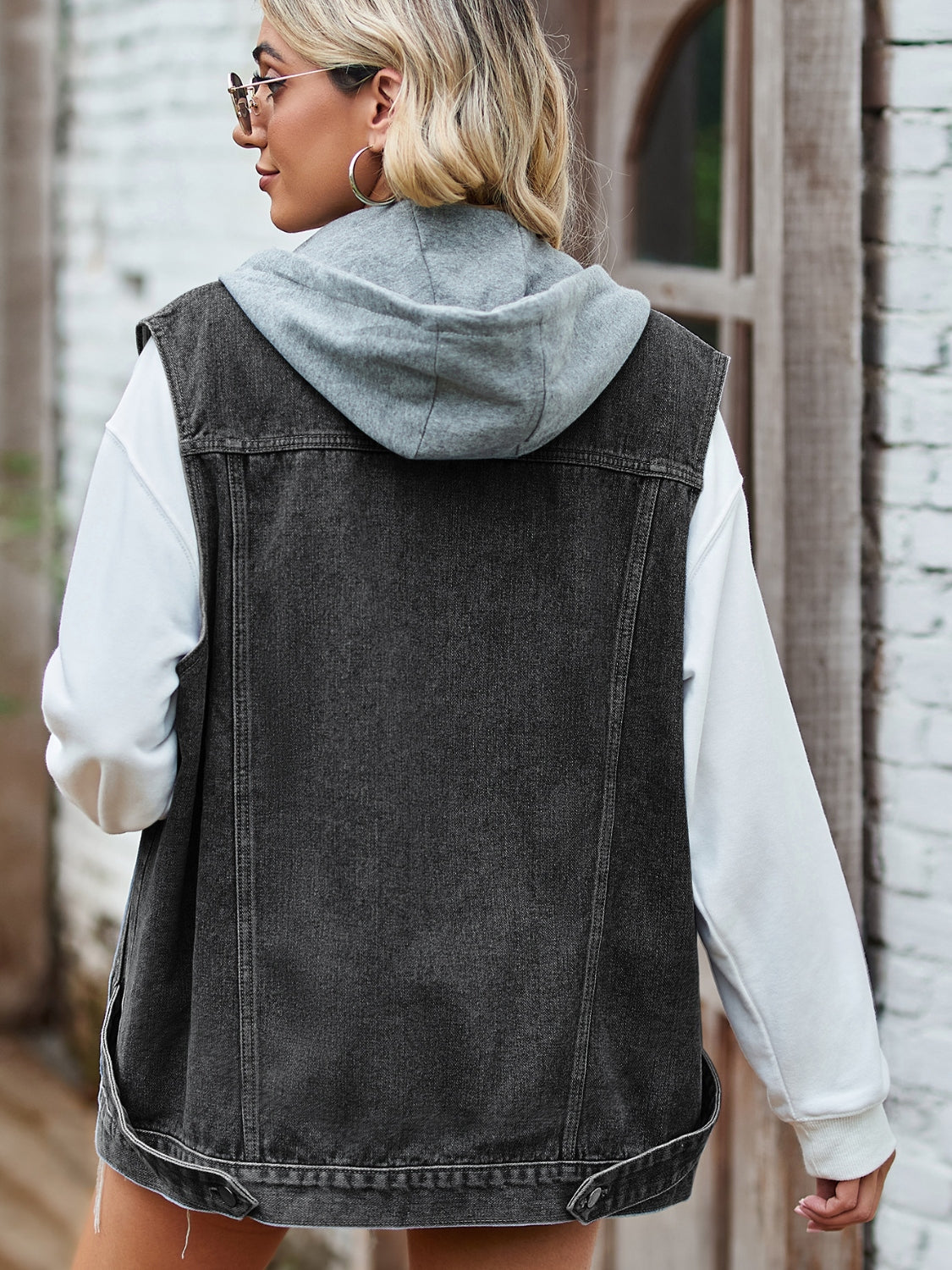Black hooded denim vest with patch pockets, worn over a white hoodie.