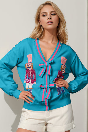 Cerulean acrylic cardigan with sequin nutcracker embellishments and pink bow details.