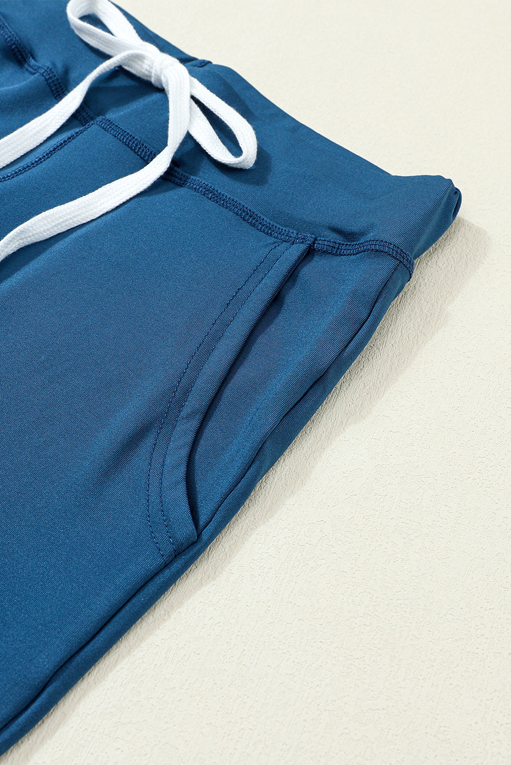 Slim-fit dark blue drawstring joggers with white tie and side pocket detail.