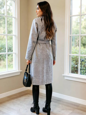 Gray textured double-breasted trench coat with waist tie, buttoned cuffs, and black handbag.