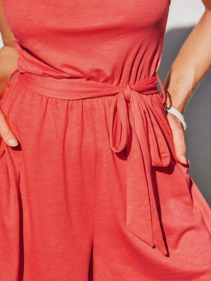 Coral asymmetrical knot-waist romper with pockets and tie belt.