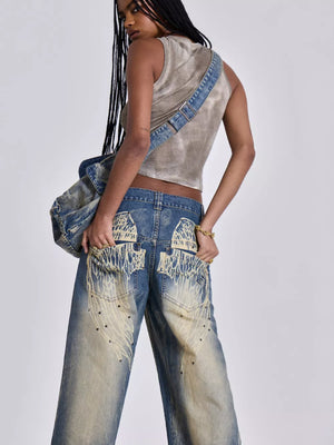 Blue wide leg jeans with vintage wash, studded details, and distressed graphic pockets.