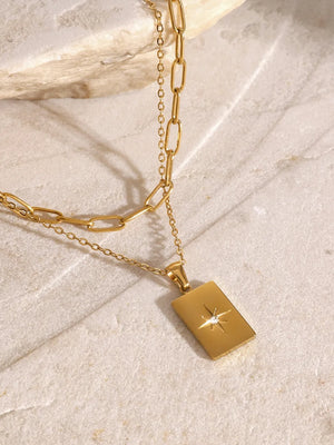Gold layered chain necklace with celestial starburst pendant and crystal accent.