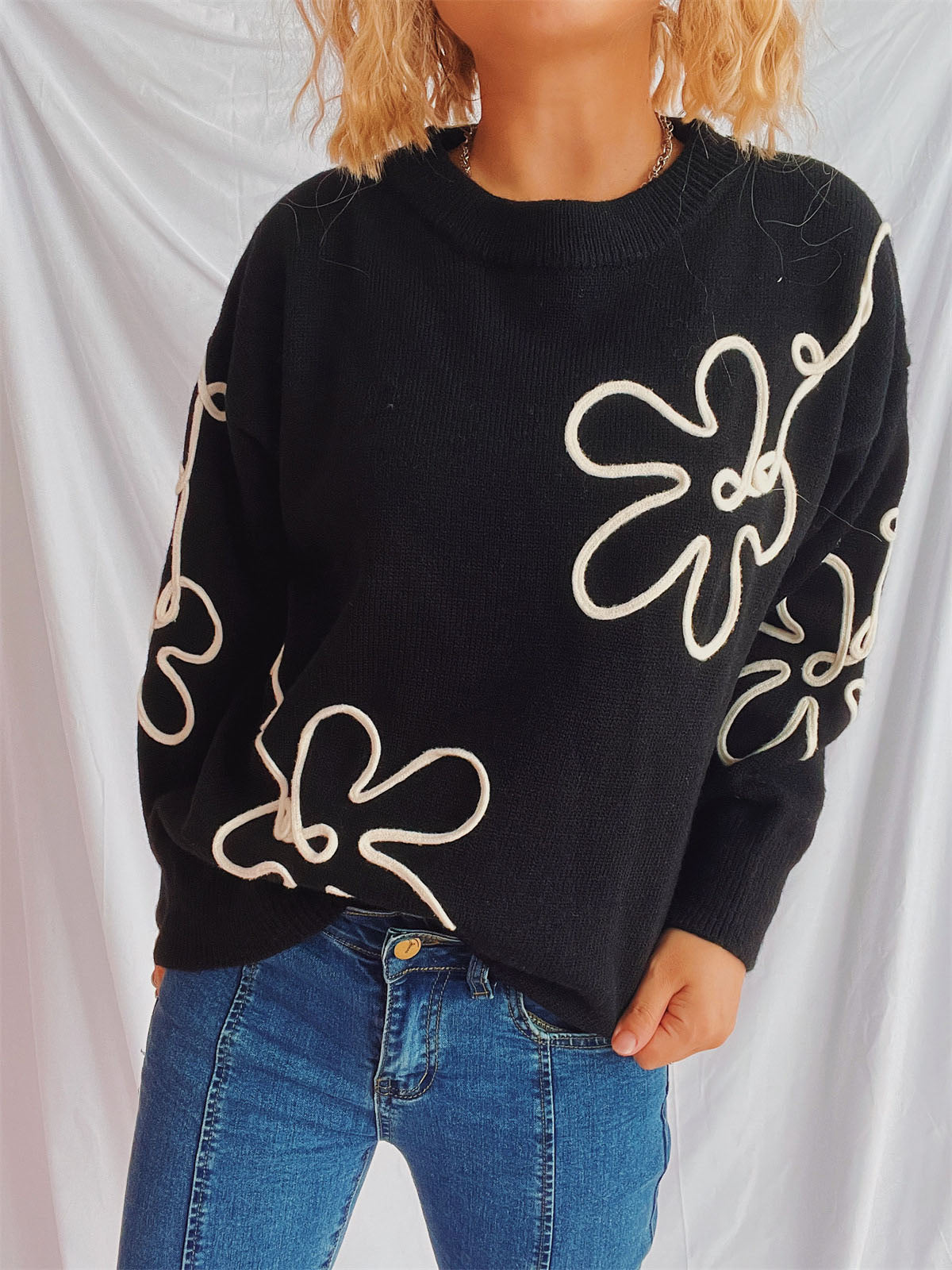 Black acrylic knit sweater with white floral outline pattern and crew neck.