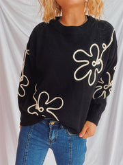 Black acrylic knit sweater with white floral outline pattern and crew neck.