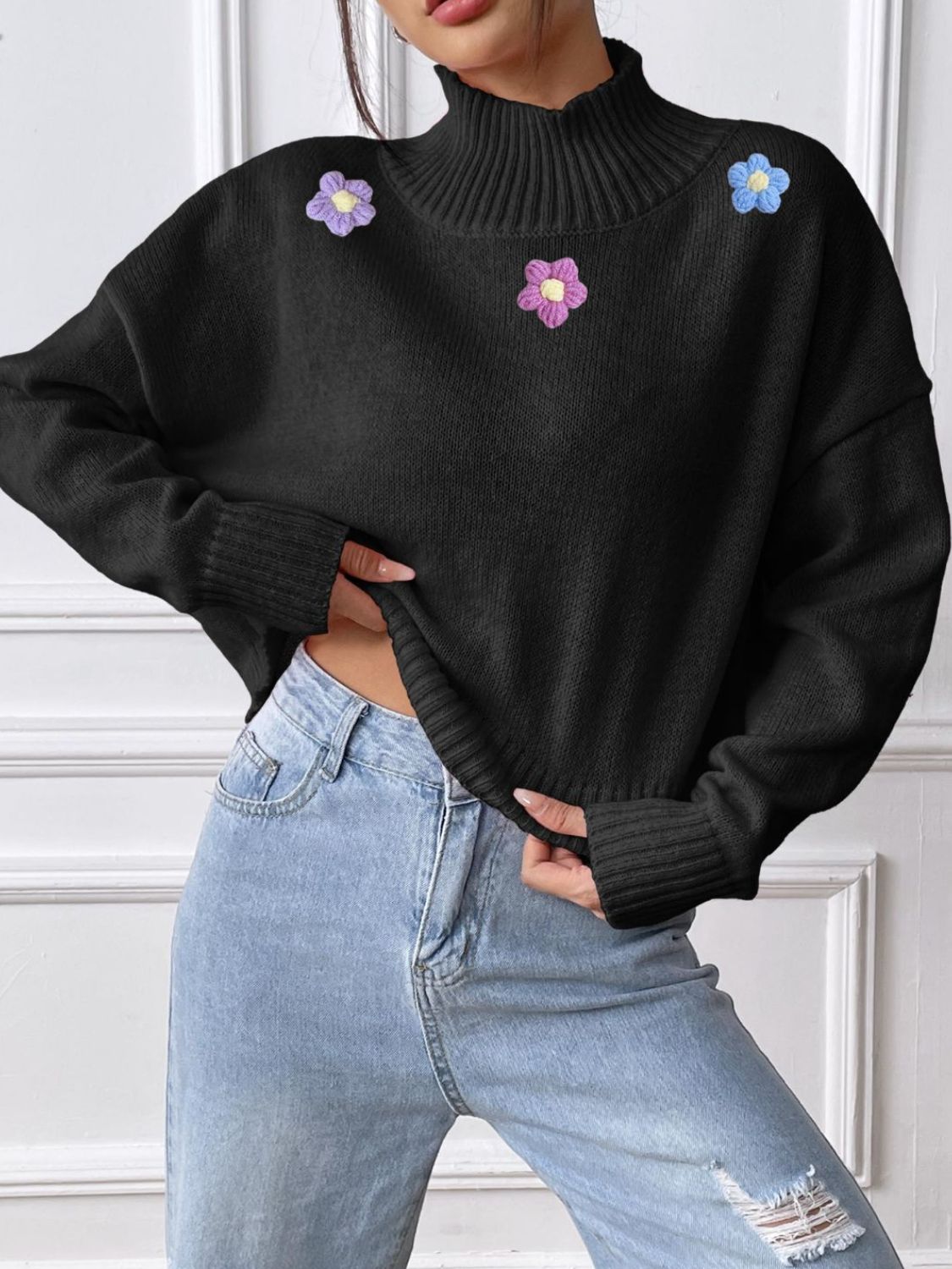 Black cropped turtleneck knit sweater with embroidered floral appliques and ribbed cuffs.