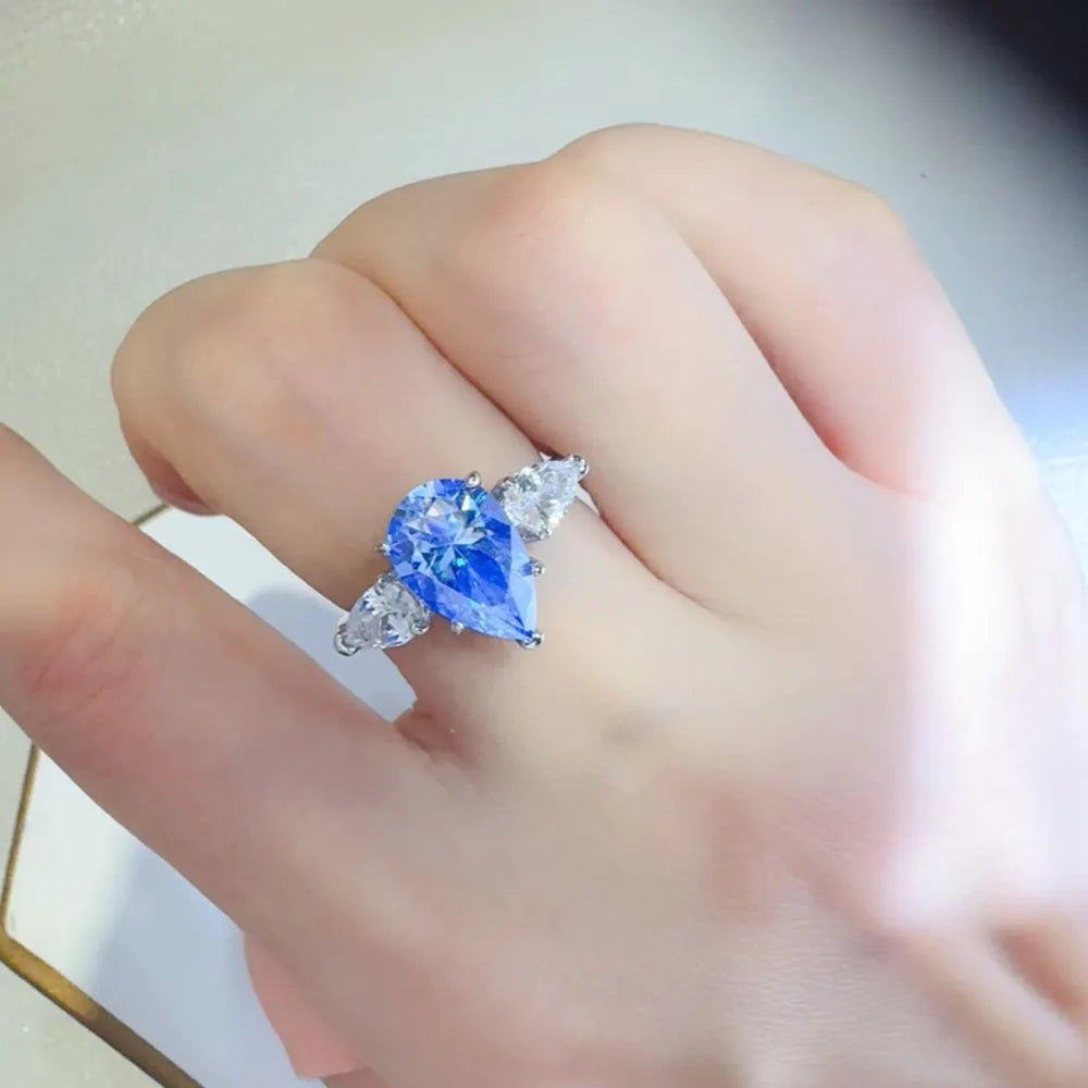 Silver ring with a blue pear cut moissanite and two side stones.