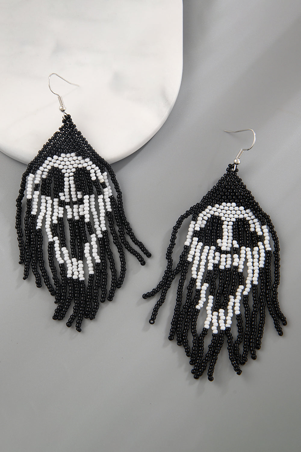 Beaded skull fringe earrings in black and white with dangling strands.