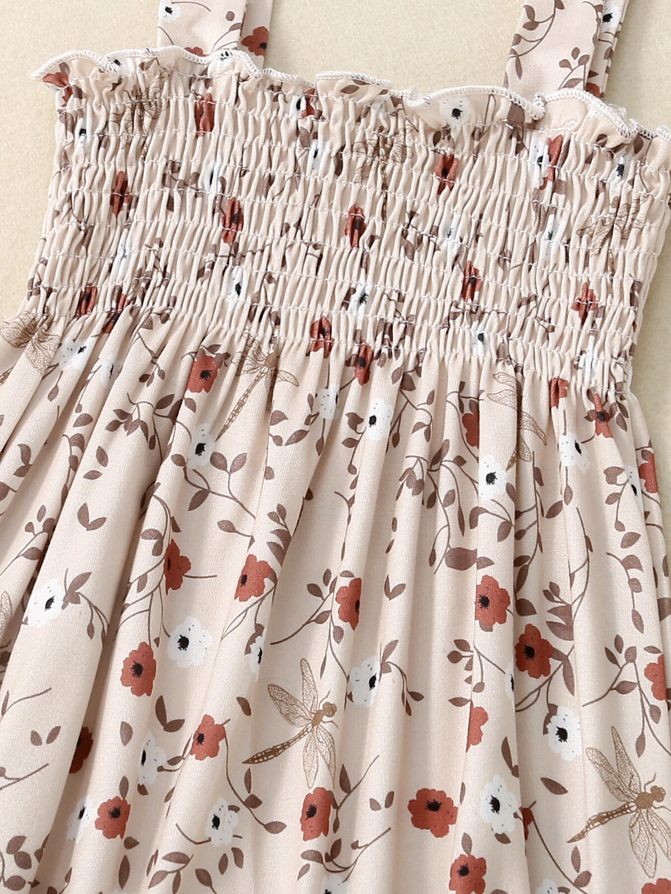 Baby jumpsuit with smocked bodice, floral print, and dragonfly accents.
