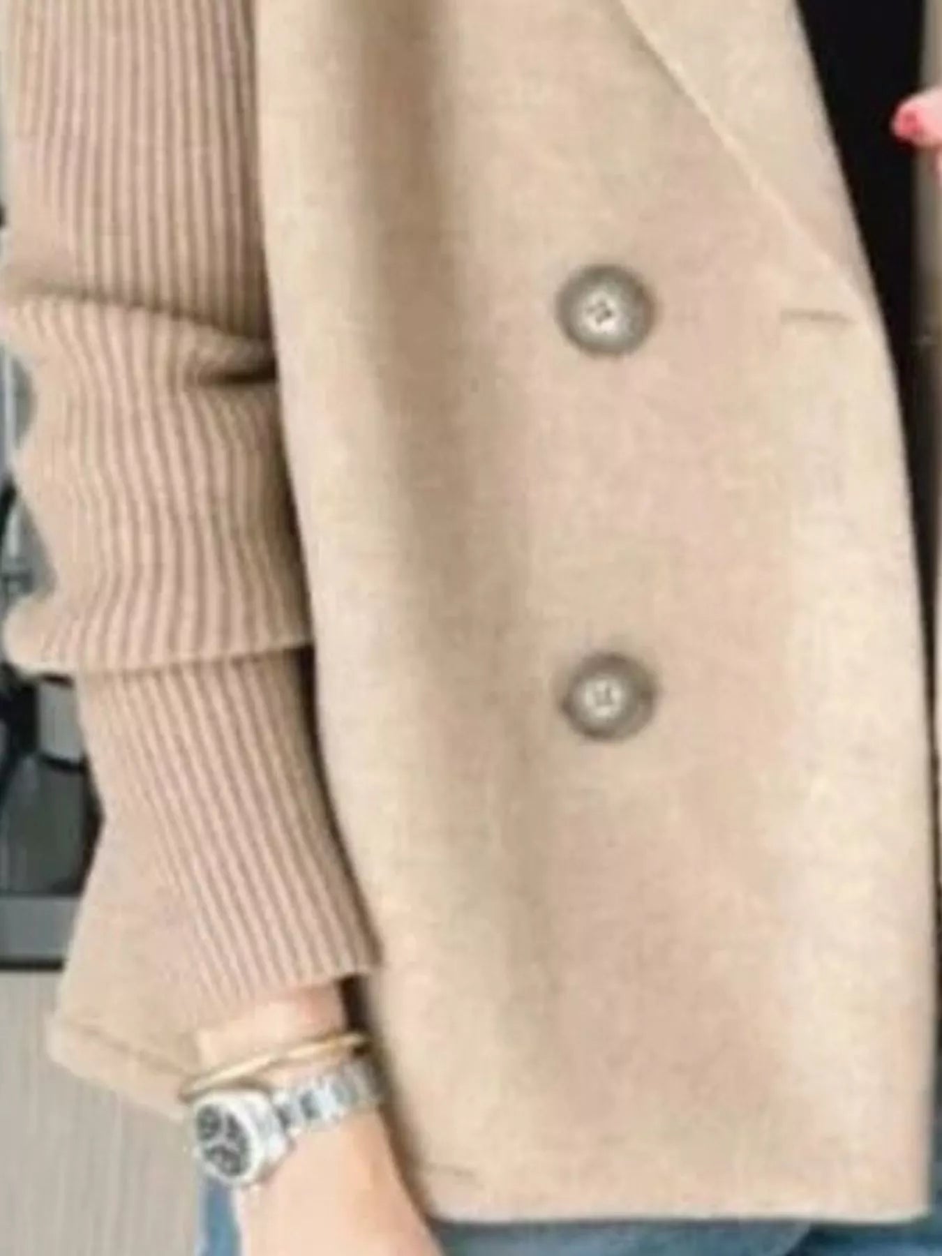 Tan double-breasted knit sleeve outerwear with two buttons, worn with a ribbed sweater and watch.